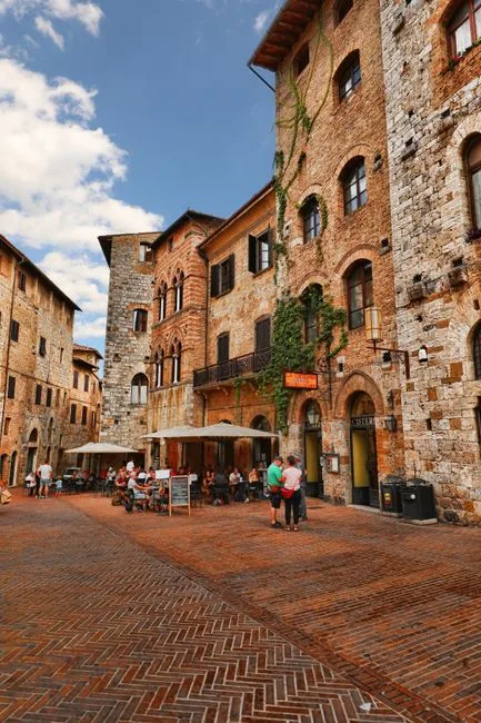 Cobblestone square in San Gimignano lined with cafés and stone buildings