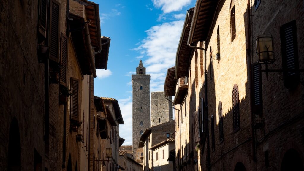 Narrow sunlit San Gimignano street framed by stone buildings and tower