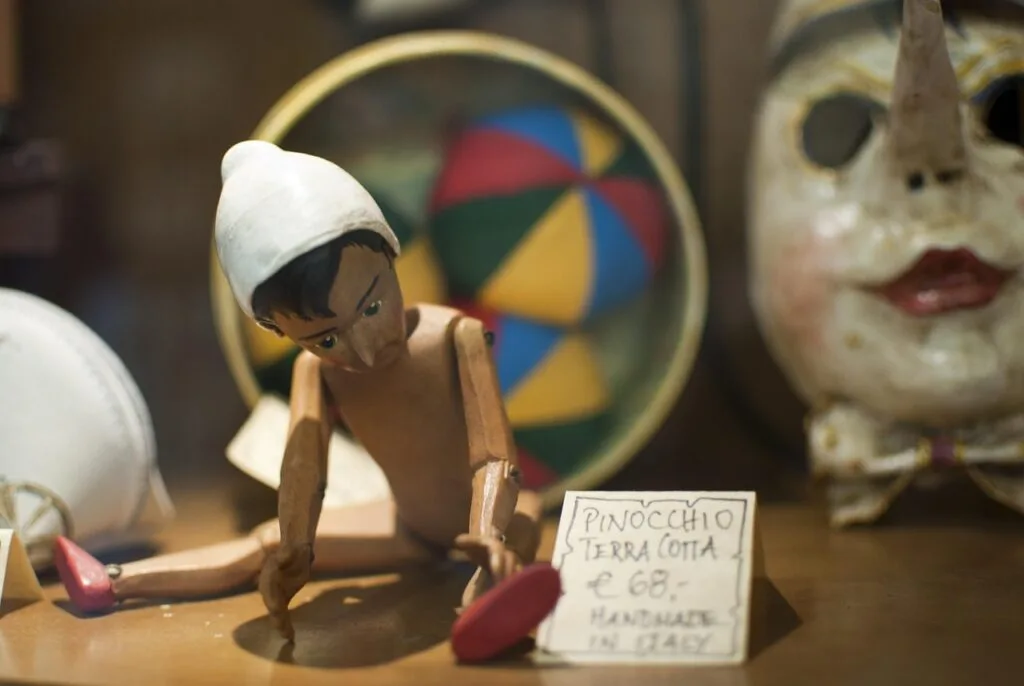 Handmade wooden Pinocchio puppet displayed with handwritten price tag in Collodi