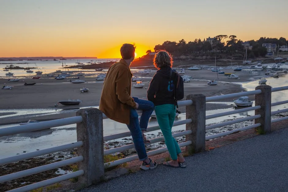 Couple sitting on railing watching sunset over beached boats and harbor