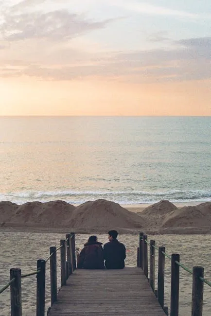 Couple sitting on wooden boardwalk facing calm sea at sunset