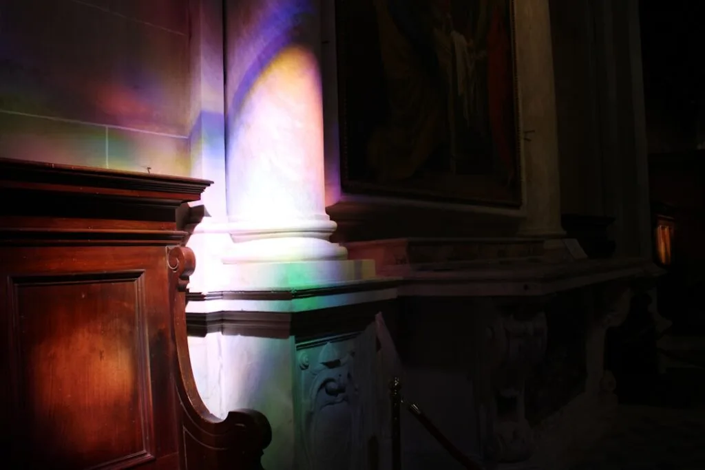 Rainbow-streaked marble column illuminated by stained glass inside Lucca church