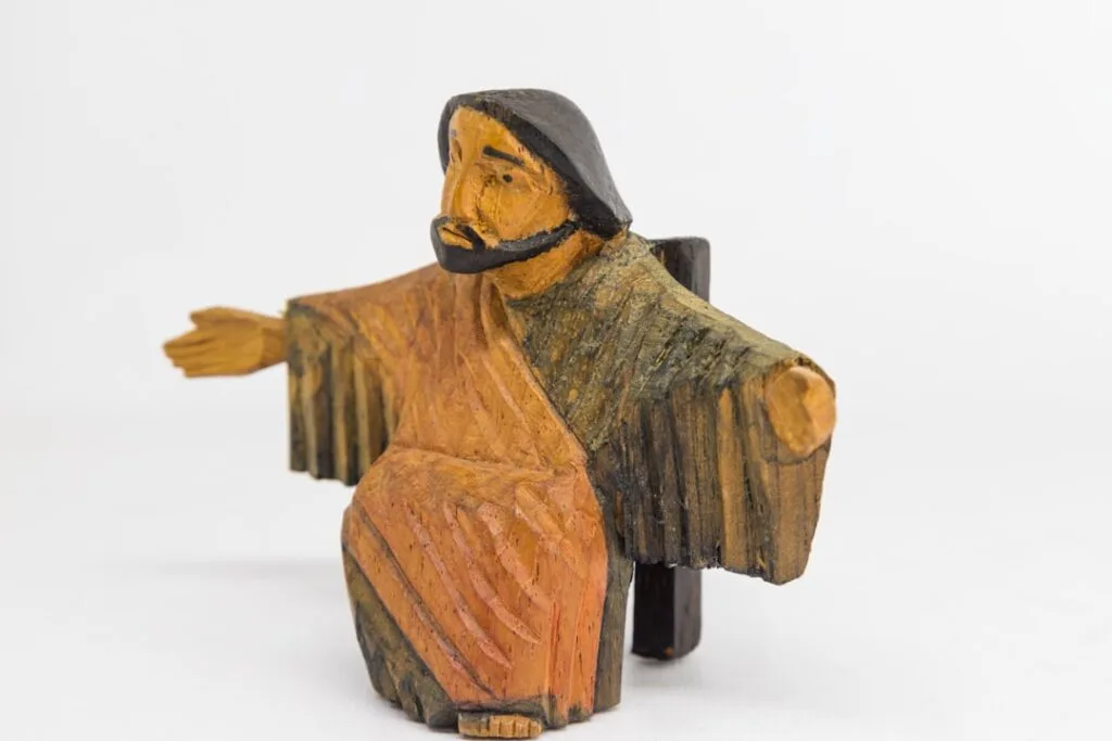 Carved wooden Christ figure with outstretched arms on white background