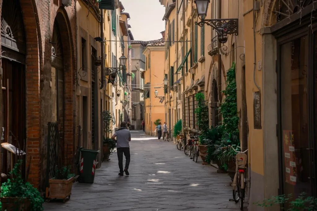 Narrow sunlit Lucca street lined with bicycles, potted plants, pedestrians