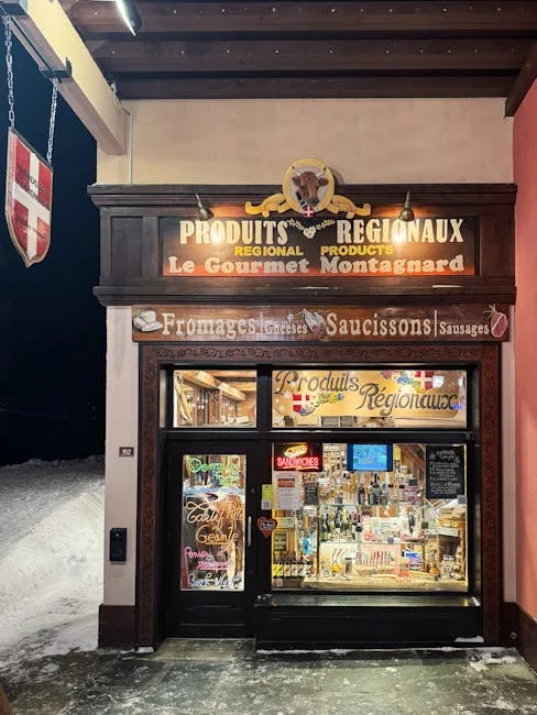 Small illuminated regional grocery storefront displaying cheeses and sausages at night