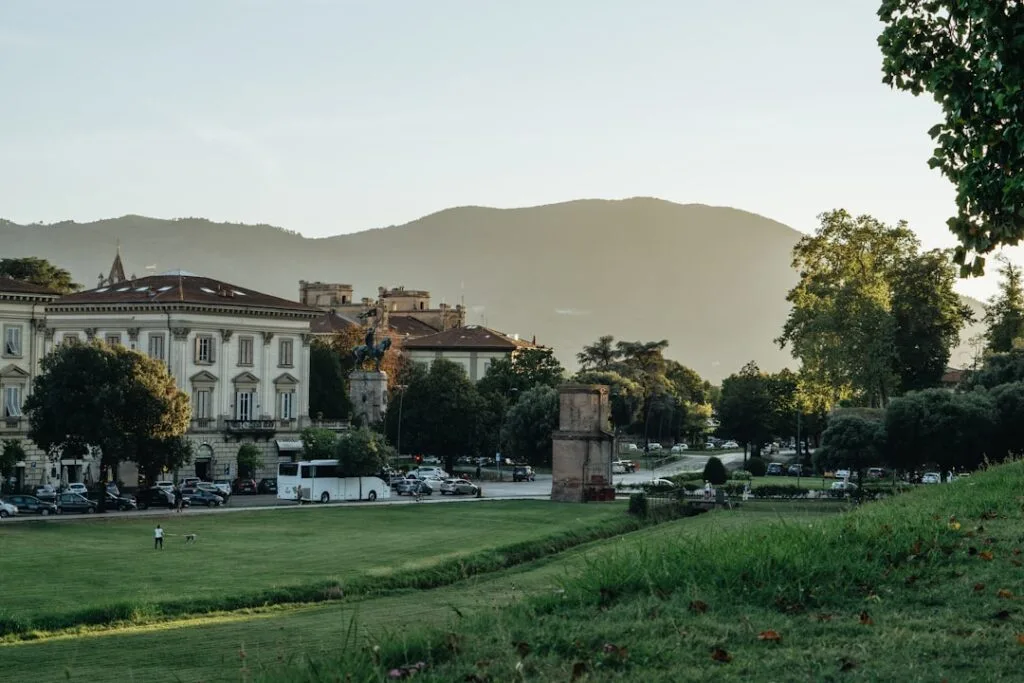 Green lawn outside Lucca city walls with people and hills.