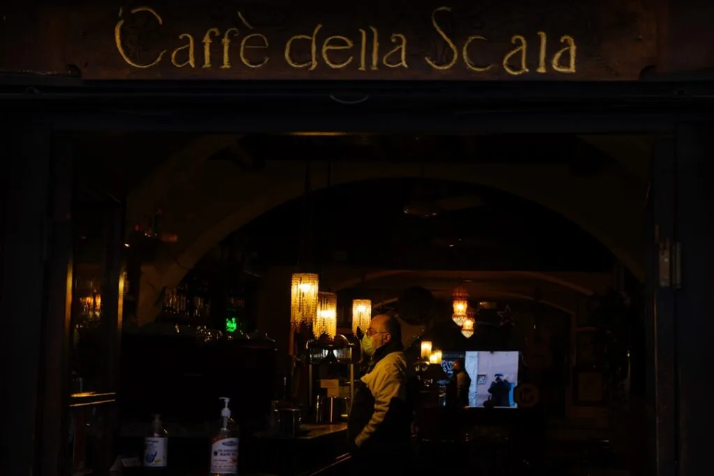Dimly lit Lucca cafe interior with barista wearing a mask.