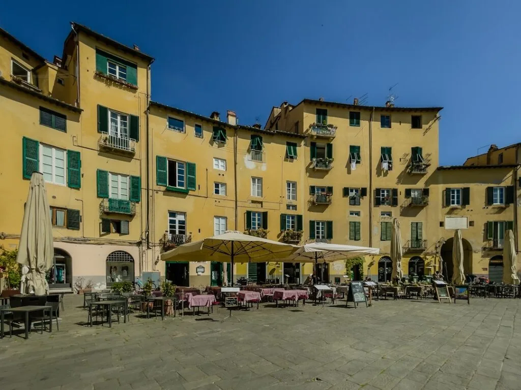 Sunny Lucca piazza with yellow buildings, umbrellas and outdoor café seating