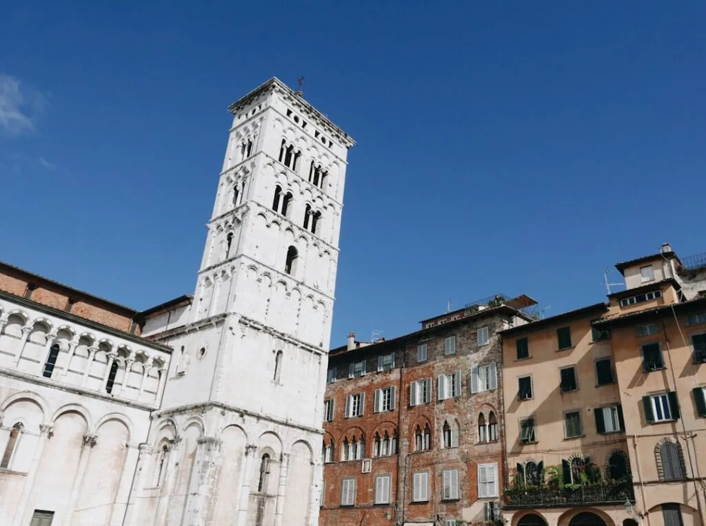 White cathedral tower in Lucca beside weathered brick residential façades