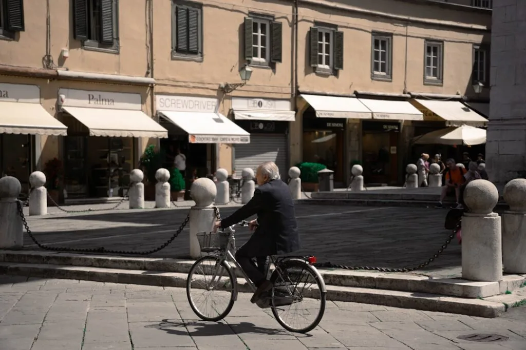 Elderly man riding a bicycle past stone bollards in Lucca.