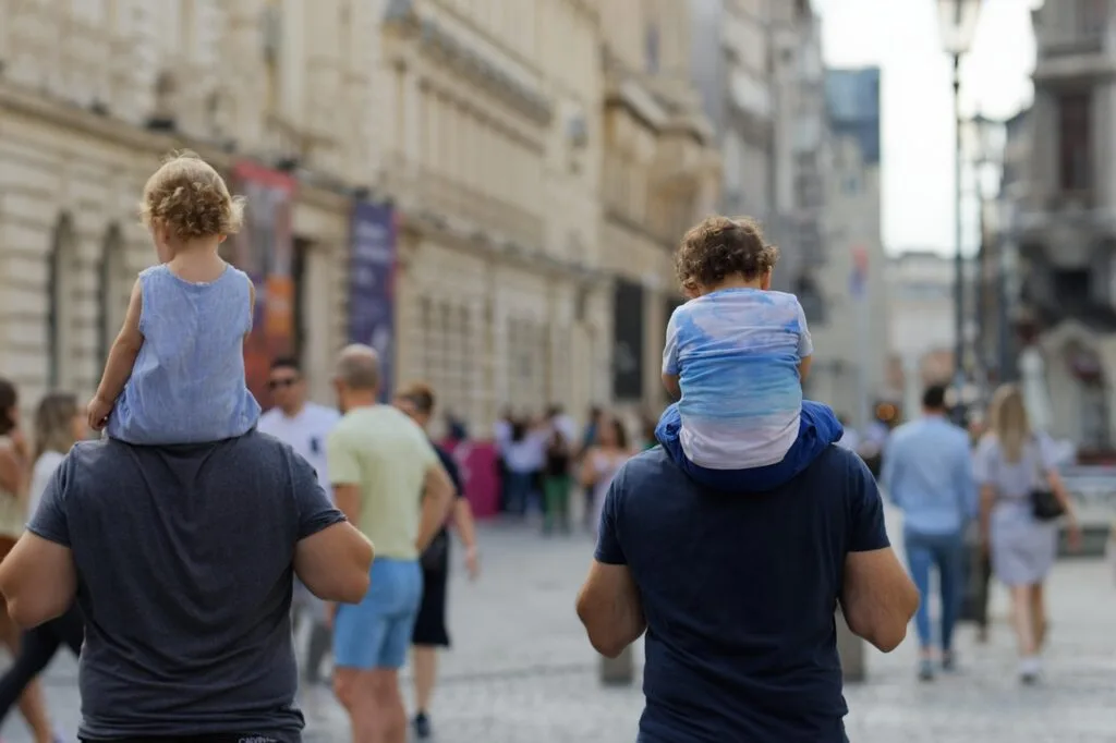 Deux adultes portant des enfants sur les épaules dans une rue animée