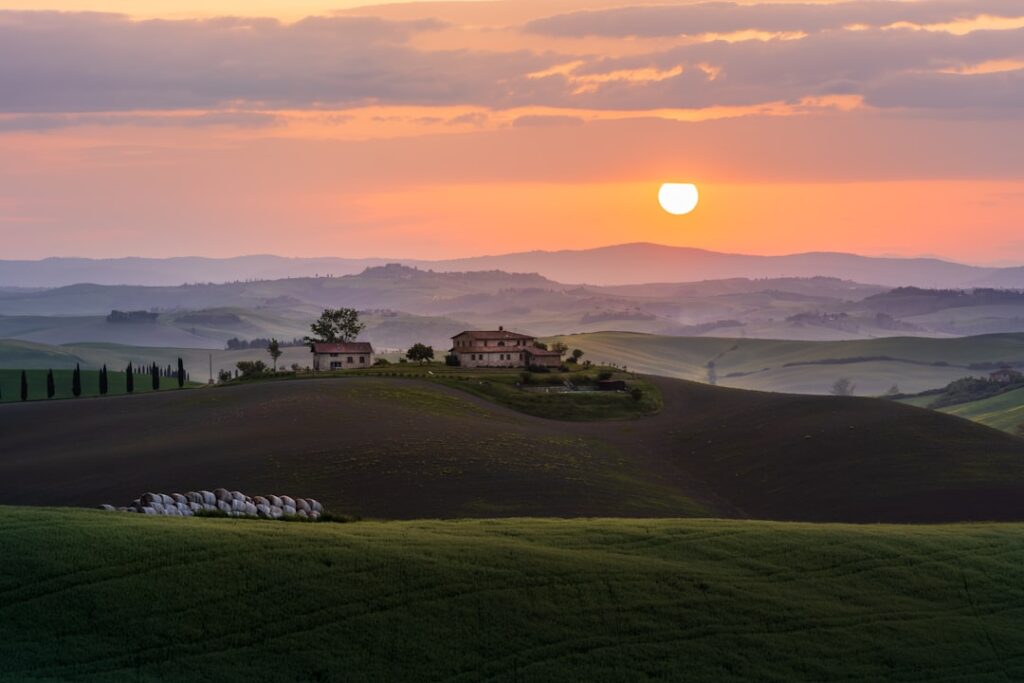 Farmhouse on a hill at sunrise over rolling Tuscan countryside.