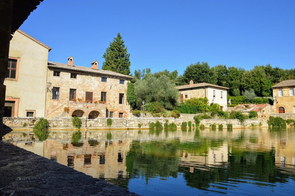 Antichi edifici in pietra riflessi nella vasca termale di Bagno Vignoni, Toscana