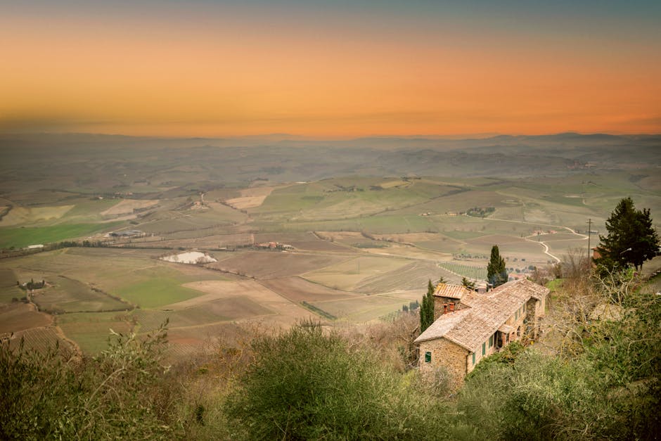 Panorama arabile dalla collina al tramonto con casale isolato in Toscana