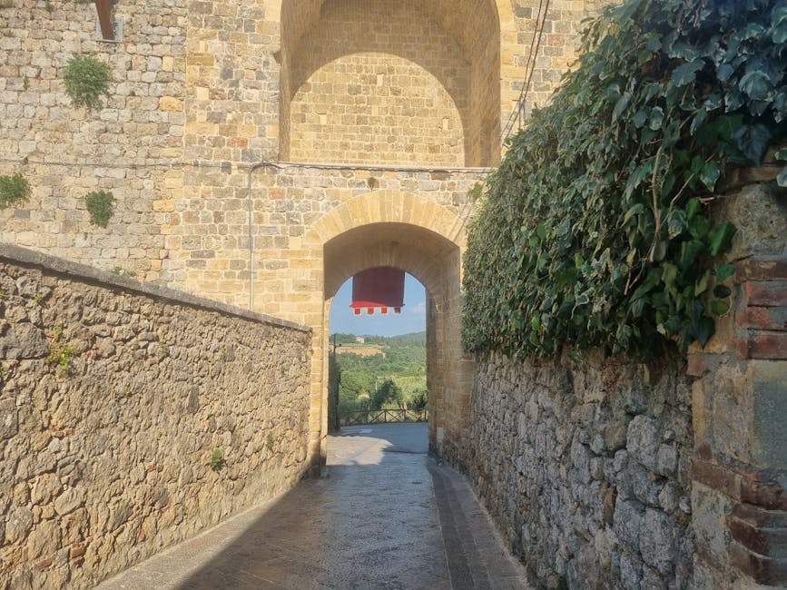 Arco di accesso tra mura in pietra con vista sulla campagna toscana