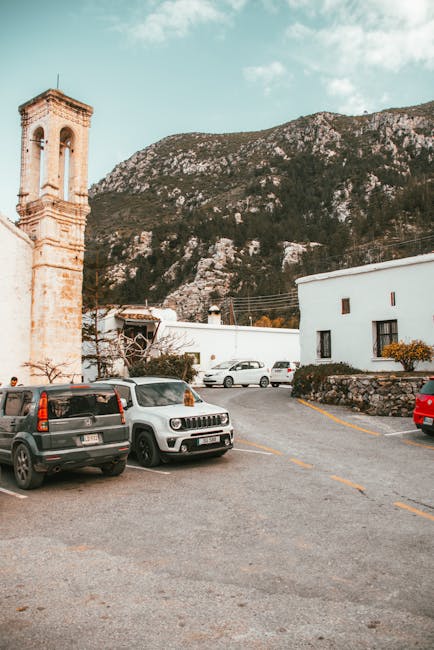 Auto parcheggiate in piazza accanto a un campanile e montagne toscane