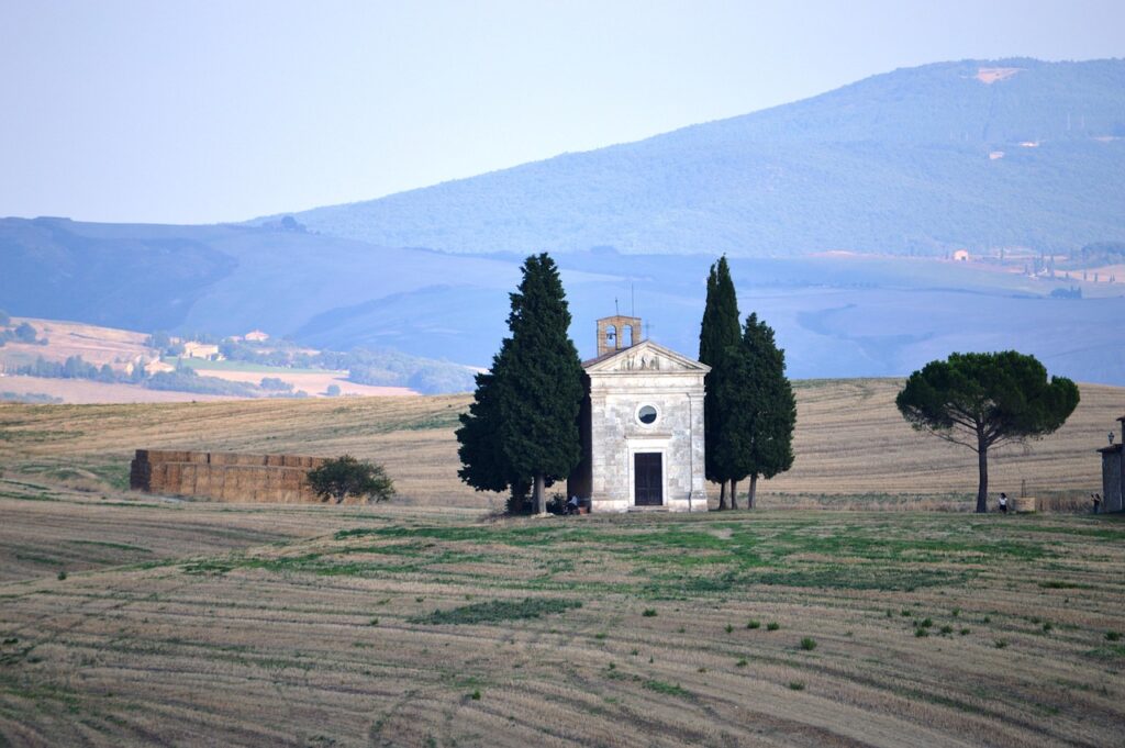 Small solitary chapel framed by cypress trees in Tuscan fields