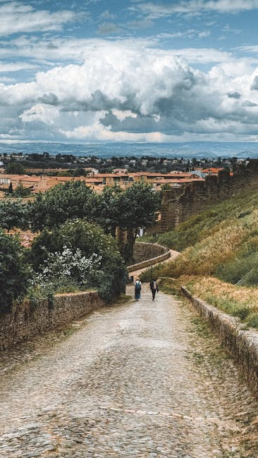 Cobblestone path toward fortified walls with two walkers in Tuscany
