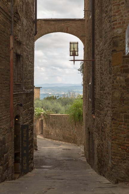 Narrow stone alley with arch and lantern opening to Tuscany