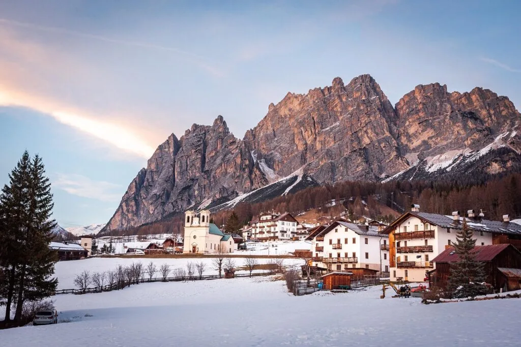 Village enneigé avec église au pied des falaises des Dolomites