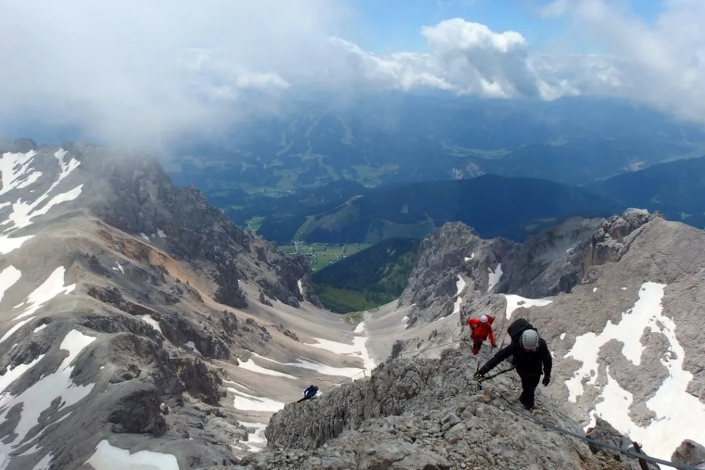 Alpinistes encordés grimpant une arête rocheuse enneigée dans les Dolomites.