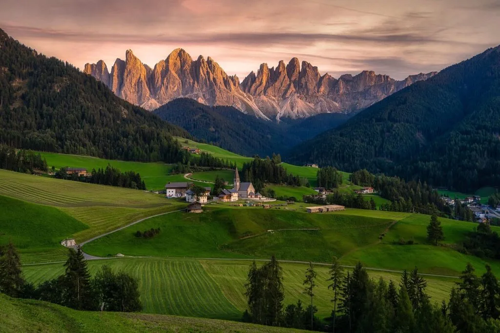 Village alpin verdoyant avec église et aiguilles rocheuses des Dolomites