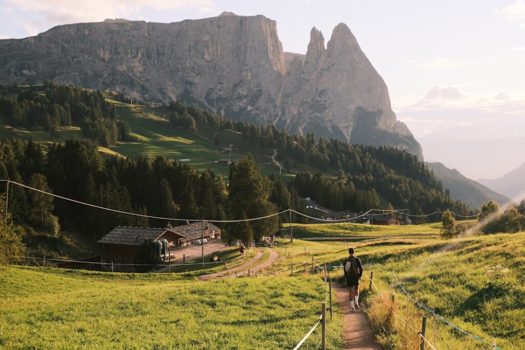 Wanderer auf Pfad durch grüne Almen, markante Dolomitenfelsen im Hintergrund