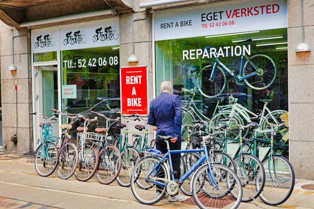 Fahrradverleih mit Reihen von Leihrädern vor Schaufenster, Mann betrachtet Fahrräder