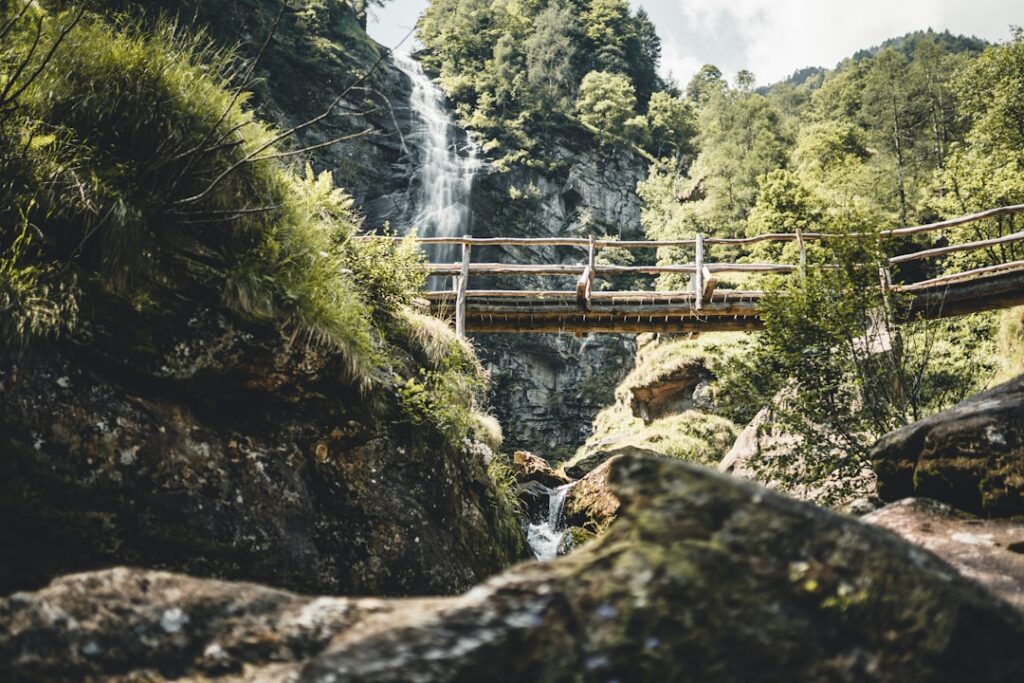 Holzsteg über wildem Bach, Wasserfall im Hintergrund der Dolomiten