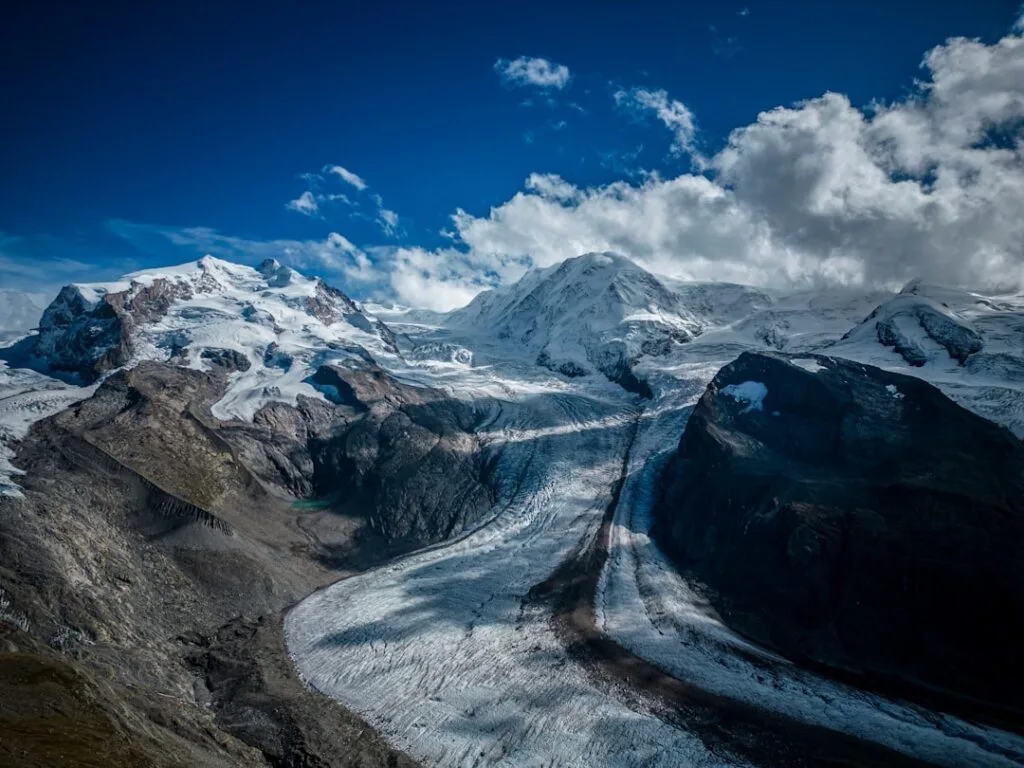 Un long glacier serpentant entre sommets enneigés sous un ciel chargé