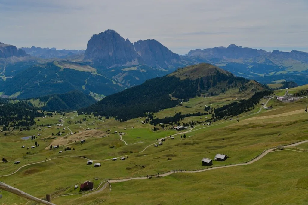 Alpiene weiden met verspreide berghutten onder een massieve Dolomietentop