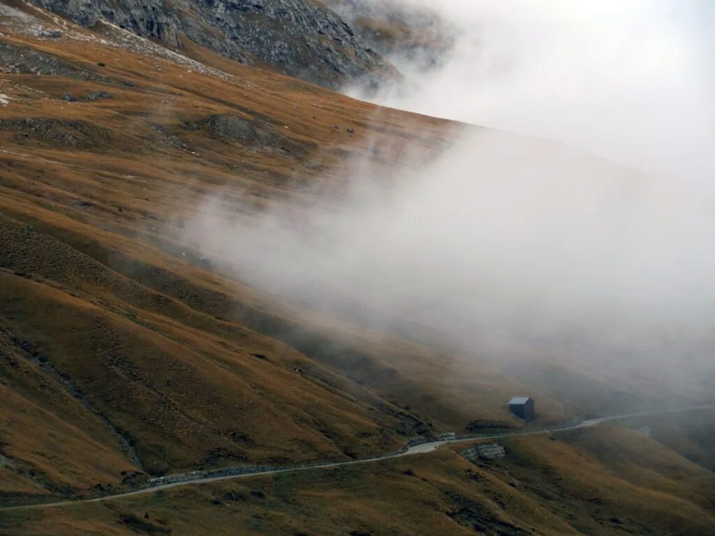 Route sinueuse et petite cabane enveloppées de brouillard sur les Dolomites.
