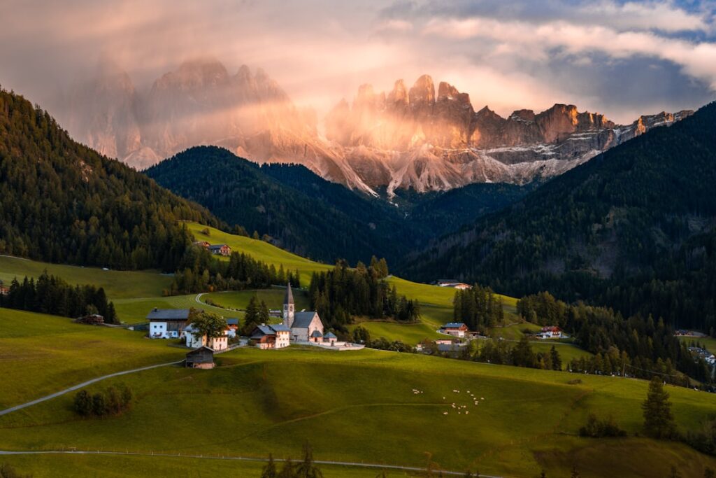 Idyllisches Bergdorf mit Kirche in grünen Wiesen, Dolomiten im Abendlicht