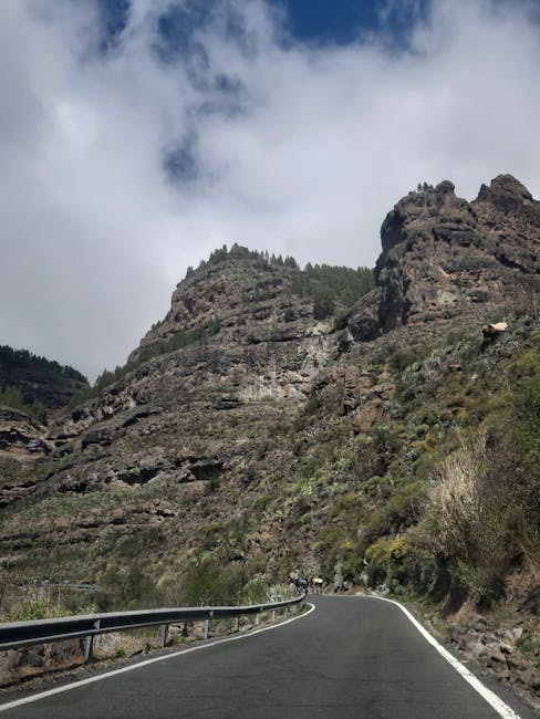 Kurvige Bergstraße in steiler Felslandschaft der Dolomiten, Radfahrer in der Ferne