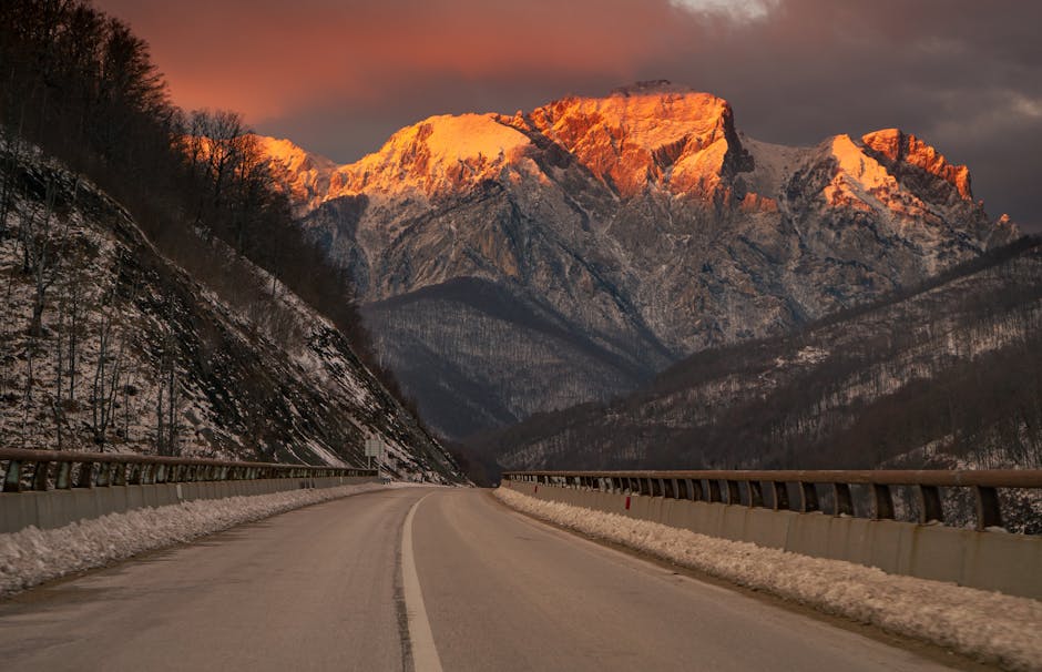 Leere Bergstraße mit Schnee, von Abendrot beleuchteten Gipfeln der Dolomiten