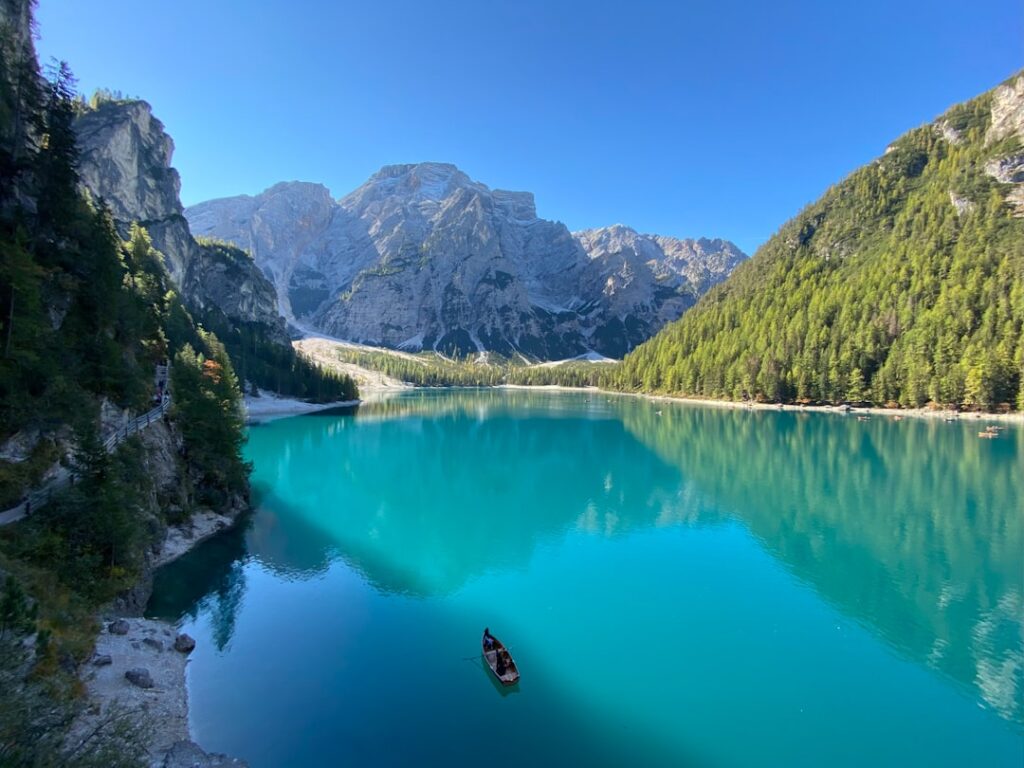 Turquoise Dolomites lake with small rowboat and surrounding pine forests