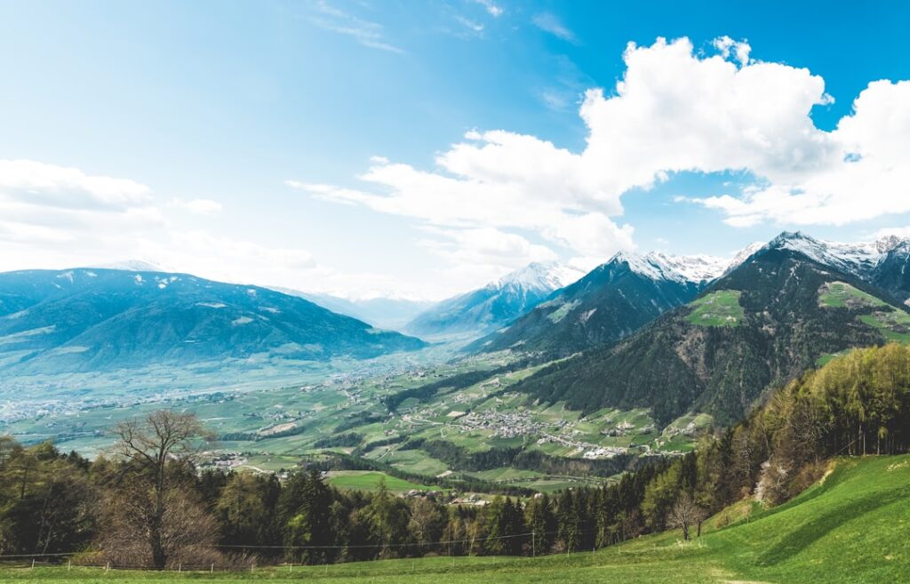 Weites Tal mit Dörfern und schneebedeckten Dolomitengipfeln unter blauem Himmel