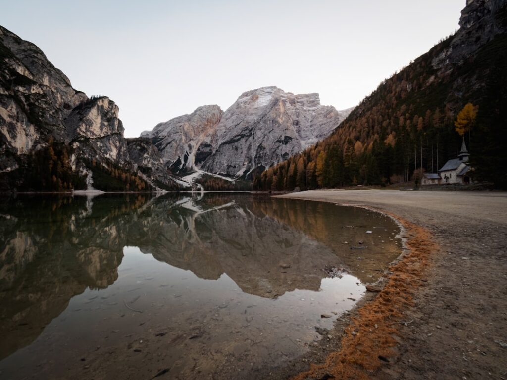 Calm lake reflecting Dolomites peaks and lakeshore church at dawn