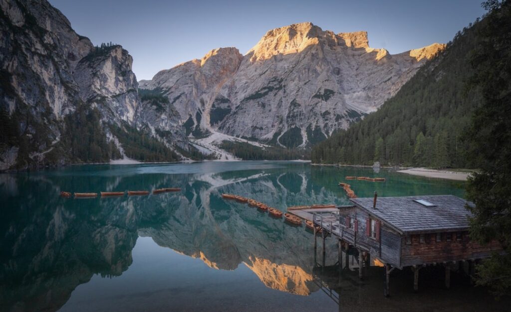 Bootshaus und Ruderboote auf stillem Bergsee mit Dolomiten-Reflexion