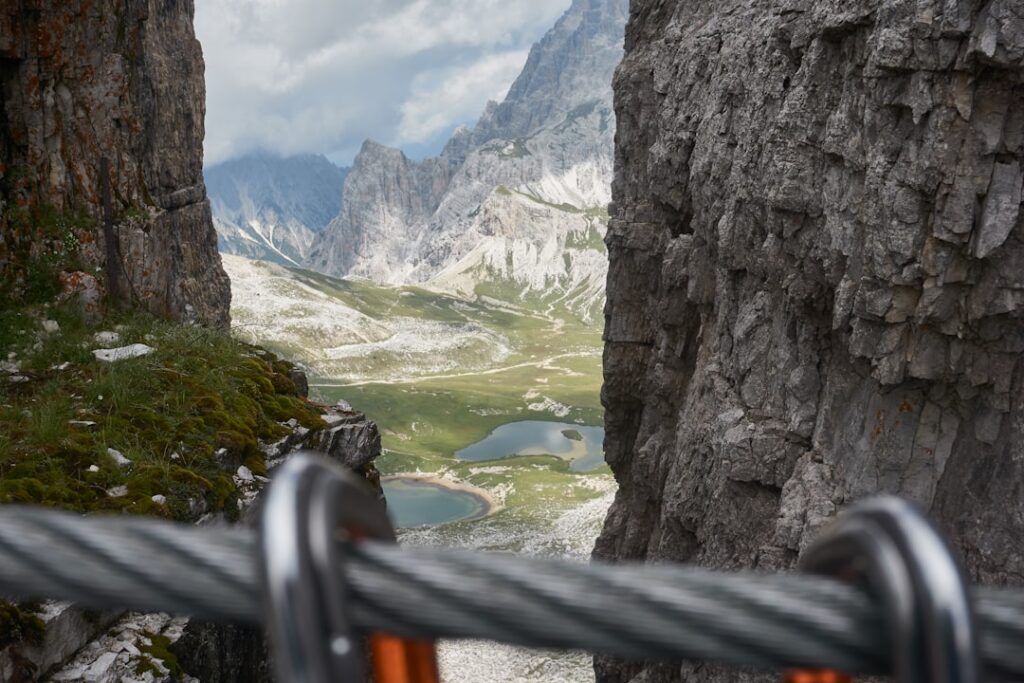 Via ferrata cable and carabiners framing Dolomites lakes and jagged peaks
