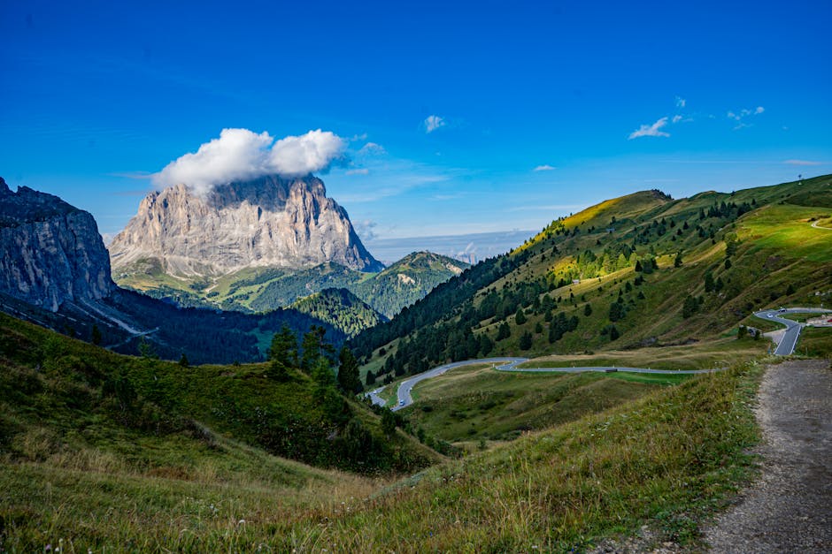 Route en lacets traversant prairies, vue sur sommet imposant des Dolomites