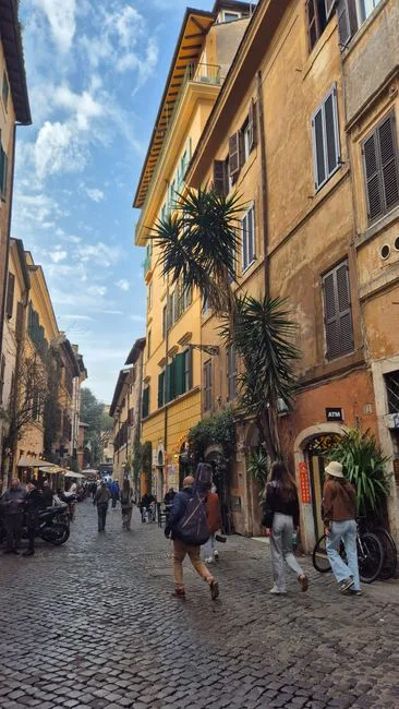 Rue pavée animée de Trastevere à Rome, façades colorées et passants.