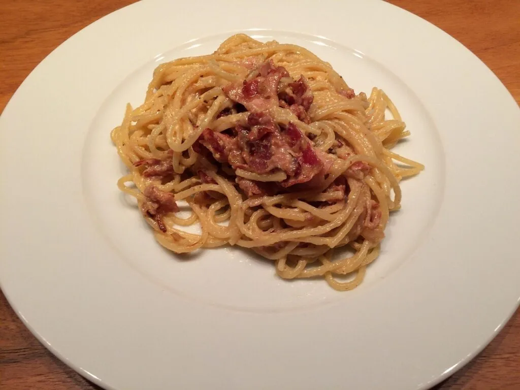 Tassée de pâtes carbonara avec morceaux de guanciale sur assiette