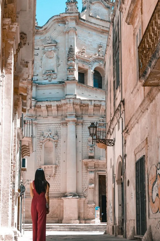 Woman in red jumpsuit admiring ornate Baroque church facade in Lecce