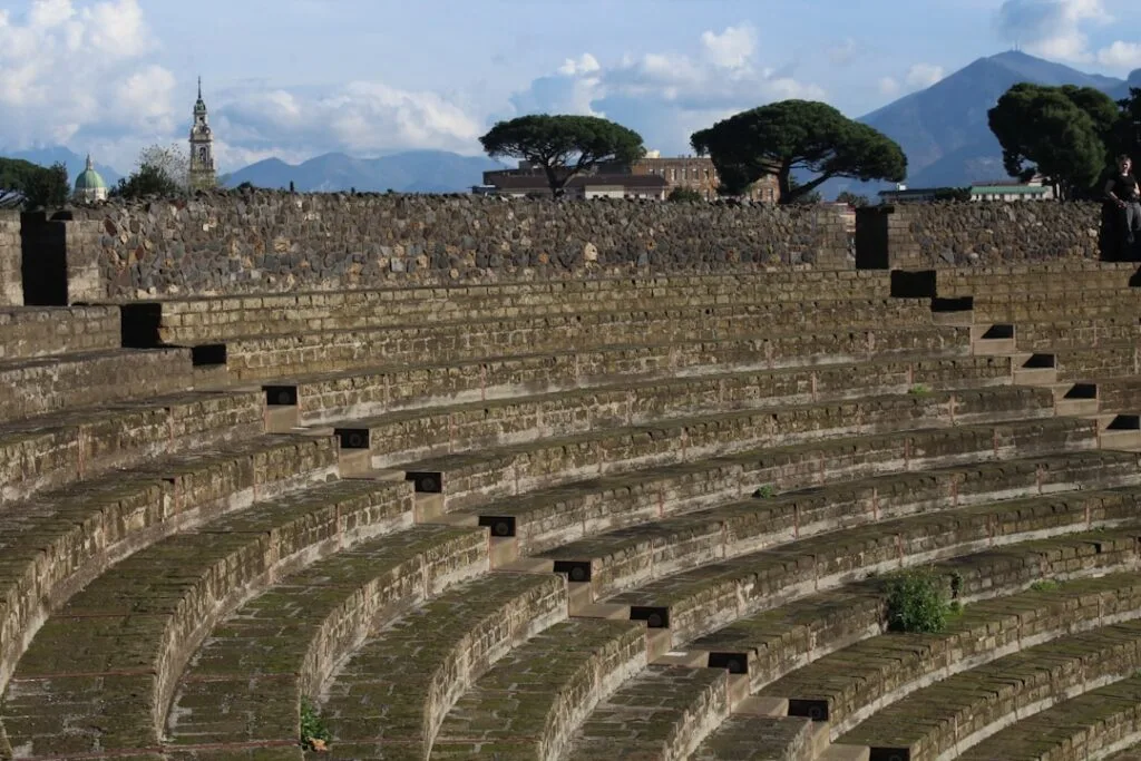 Curved ancient stone amphitheater seating rows under a cloudy mountain sky