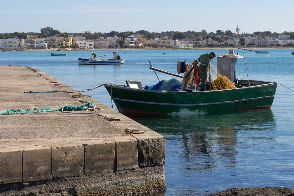 Green fishing boat with fishermen mending nets at Lecce harbor