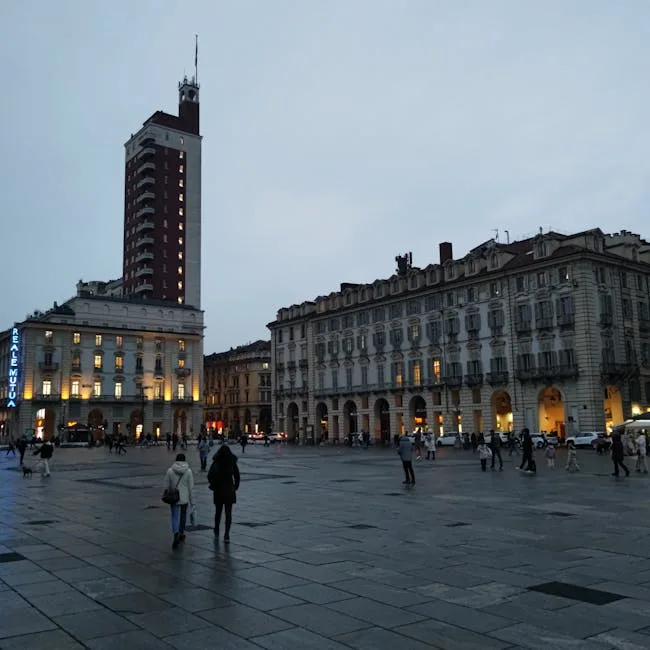 Belebter Platz in Turin mit hohem Turm und Arkaden im Abendlicht