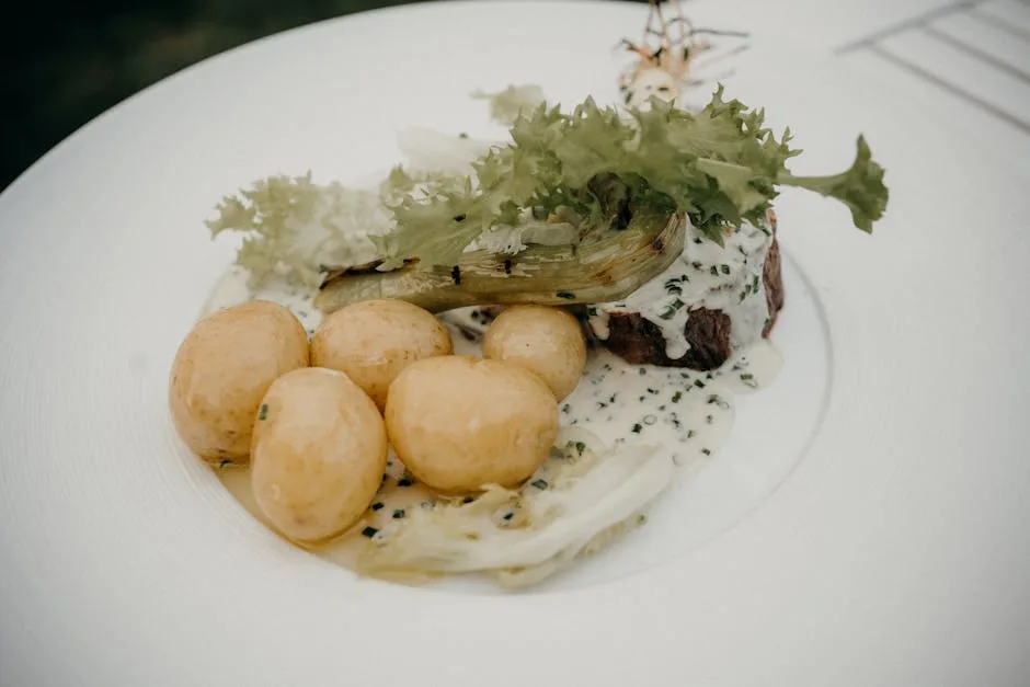 assiette blanche avec pommes de terre nouvelles, sauce onctueuse et jeunes feuilles