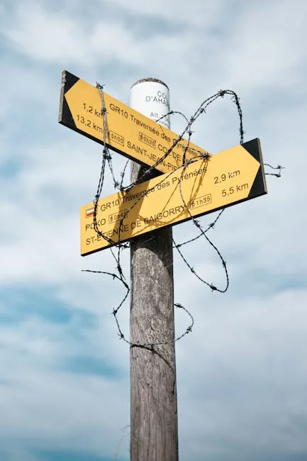 Gelbe Wanderwegschilder an einem Holzpfahl, umwickelt mit Stacheldraht