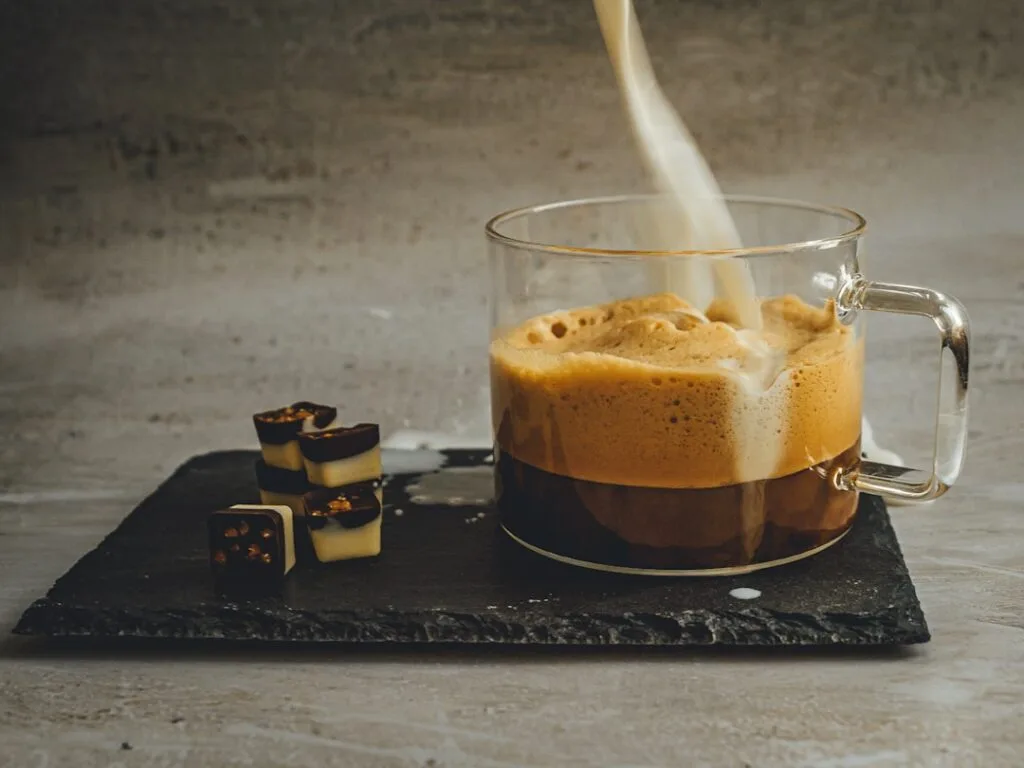 Café crémeux versé dans une tasse en verre, chocolats à côté